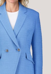 Helleblaue strukturierte Blazer mit doppelreihigem Design, silbernen Knotenknebeln und Reverskragen. Glatte weiße Innenlage sichtbar.