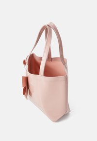 Sac fourre-tout rose brillant avec une finition lisse, double anses et un grand accent de nœud à l'avant. Le dessus ouvert révèle un intérieur rose clair.
