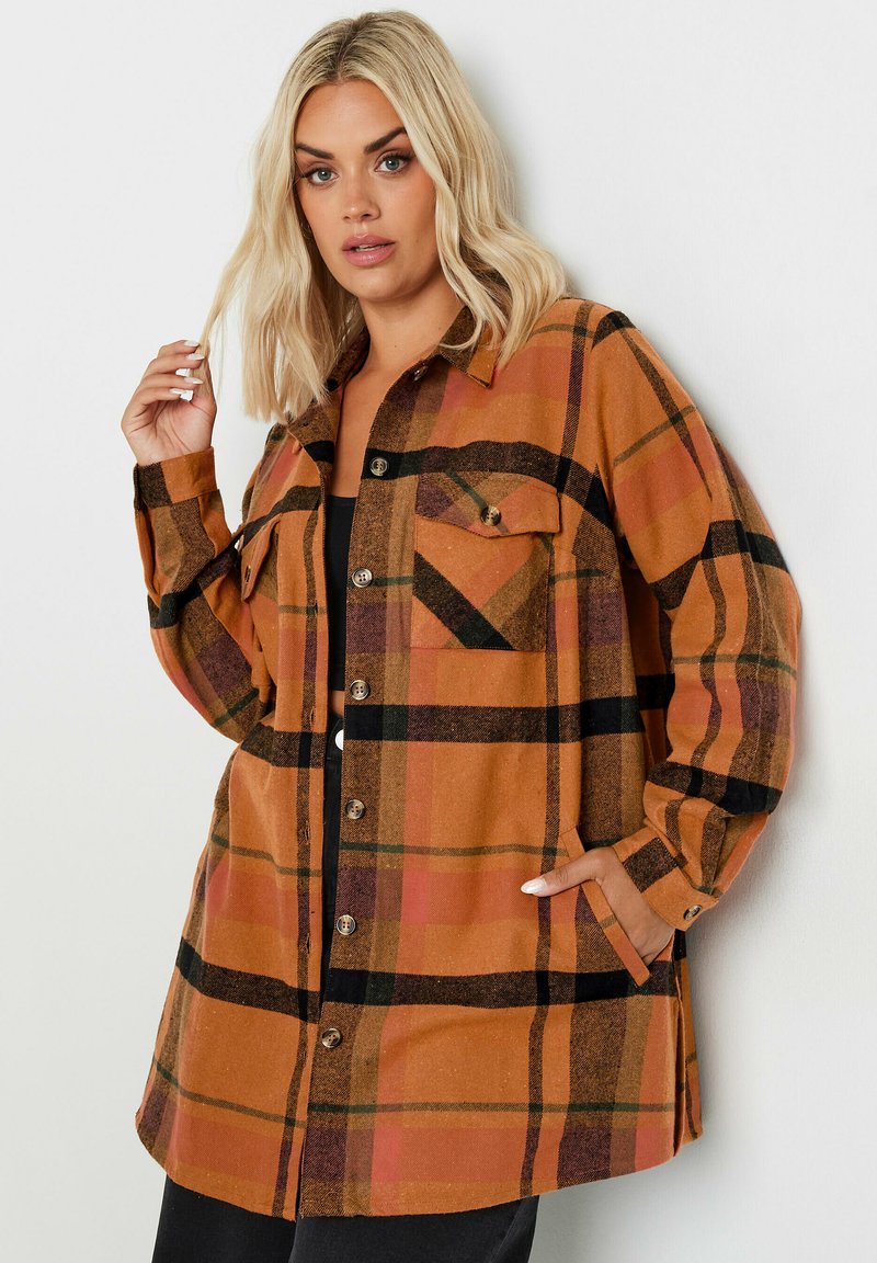 Brun rutig skjortjacka med svarta och oranga accenter, knäppning fram, två framfickor och avslappnad passform, tillverkad av mjukt tyg.