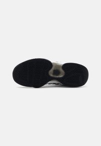 Semelle de chaussure en caoutchouc noir avec un motif de bande de roulement en zigzag, présentant une section translucide au centre et des bords incurvés pour une traction et un soutien.