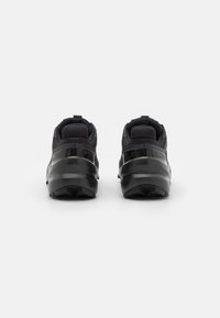 Las zapatillas deportivas negras presentan una parte superior texturizada, un talón acolchado y una suela robusta. El diseño incluye un logotipo sutil y acentos reforzados.
