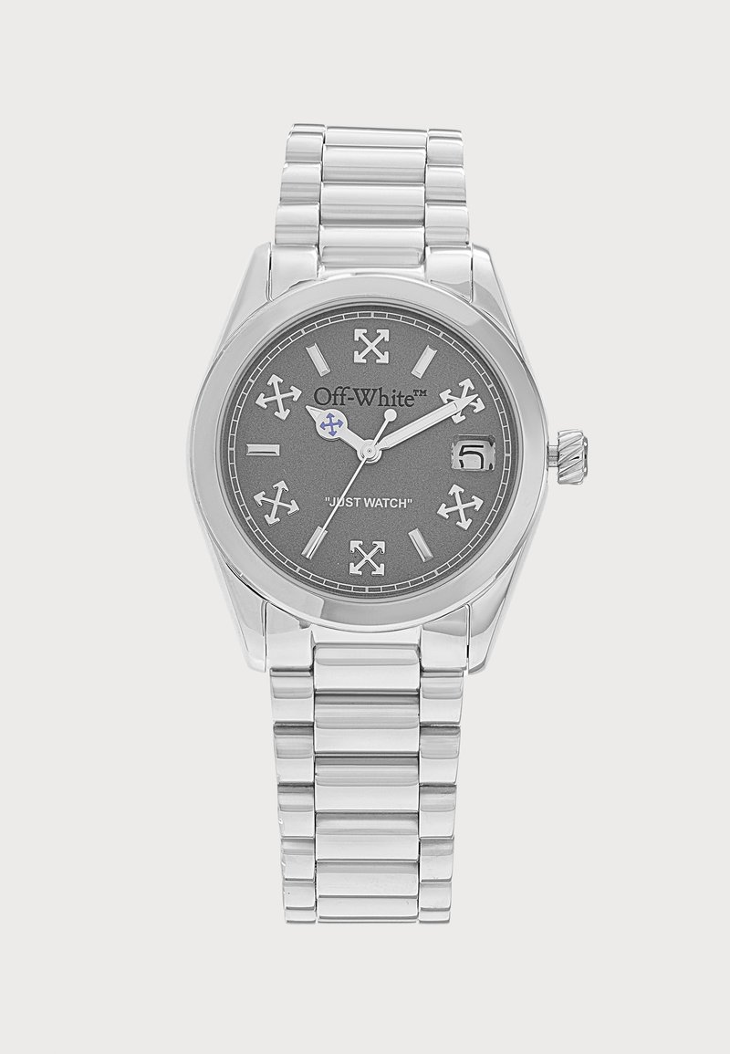 Montre-bracelet en métal argenté avec cadran gris foncé, index et aiguilles blanches, affichage de la date et texte "Off-White" et "JUST WATCH" sur le cadran.