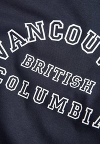 Λευκά γράμματα με περίγραμμα που γράφουν Vancouver British Columbia σε σκοτεινή υφασμάτινη επιφάνεια