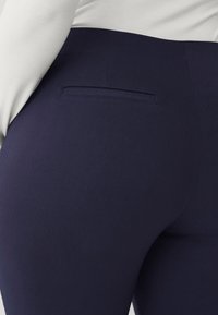 Pantaloni attillati blu navy con una texture liscia, dotati di una tasca posteriore e di un alto fascione in vita. Il tessuto sembra elastico e affusolato.
