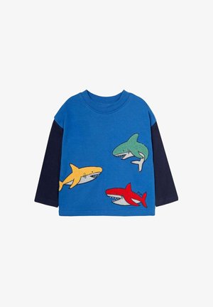 Blå langærmet skjorte med appliqué motiver af tre hajer i gul, grøn og rød på forsiden. Marineblå ærmer og ribbet halsudskæring.