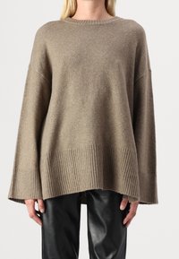 Beige oversized tröja i mjukt material, med ribbad fåll och muddar. I kombination med svarta läderbyxor för kontrast.