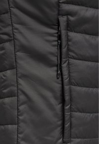 Svart isolerad jacka med diamantquiltmönster, som har en ficka med dragkedja och justering med snöre på sidan. Slät textur.