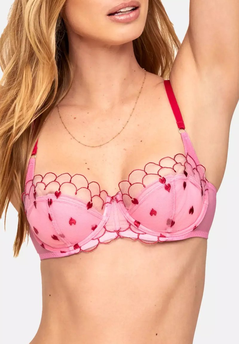 Pink underwire bra featuring sheer scalloped lace with red heart motifs and adjustable red straps. Smooth fabric with a slight sheen.