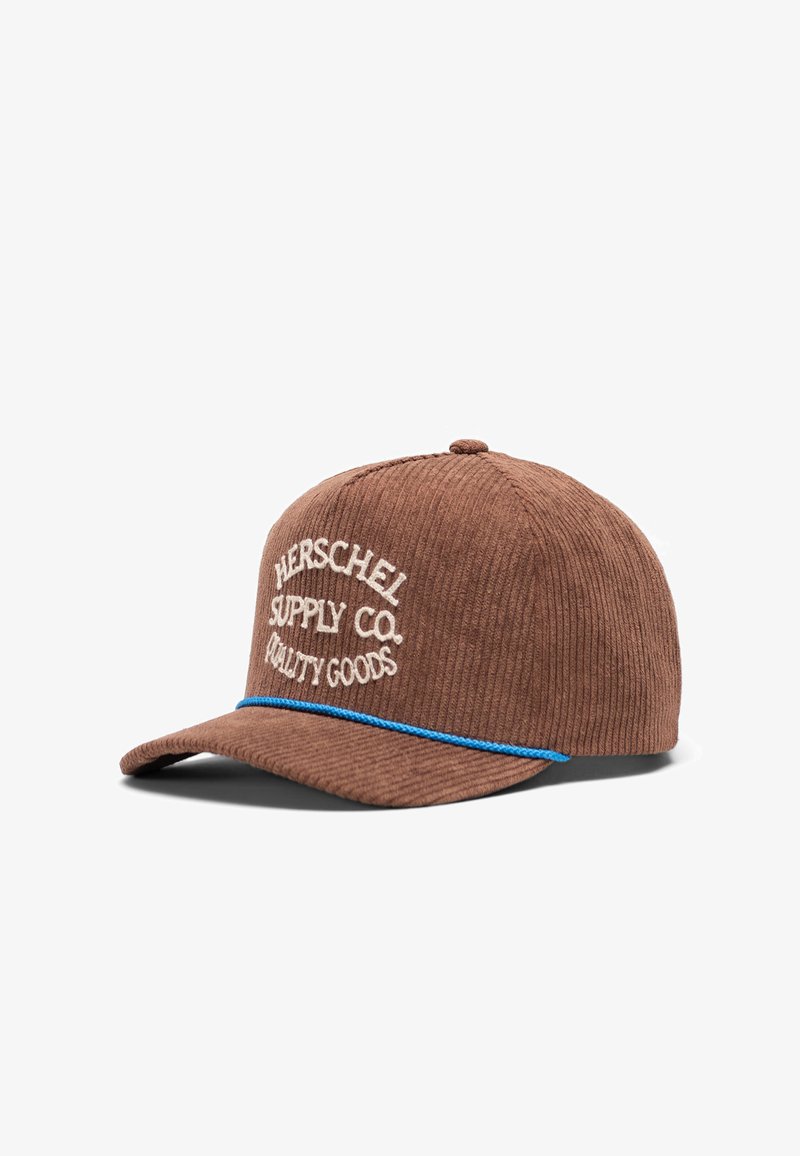 Bruine corduroy pet met een gebogen klep, voorzien van witte geborduurde tekst en een blauwe accentband boven de klep. De tekst bevat "HERSCHEL SUPPLY CO. QUALITY GOODS."