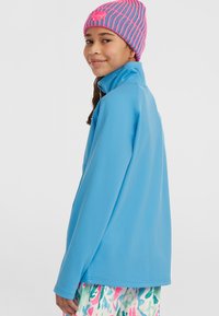 Hele sinine pikade varrukatega pullover kõrge kraega ja siledast kangast, koos roosa ja sinise triibuga beani mütsiga.