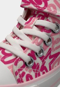 Κοντινό πλάνο ενός ροζ και λευκού αθλητικού παπουτσιού με λευκά κορδόνια και ασημένιες τρύπες, σε λευκή λαστιχένια σόλα.