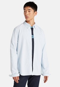 Lichtblauw, knoopsluiting overhemd met lange mouwen en een kraag, gedragen over een donkermon tshirt. Heldere stof met een gladde textuur.