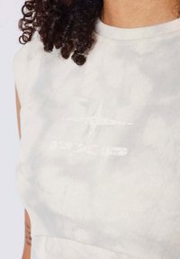 Crop top en tissu doux et léger. Présente un motif tie-dye dans des tons de gris doux et un logo graphique blanc sur la poitrine.