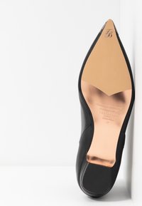 Semelle d’un talon haut pointu noir présentant des détails beige et en or rose métallisé avec le logo Ted Baker et la taille 37.