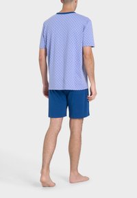 Camicetta azzurro chiaro a maniche corte con un motivo a pois e colletto a contrasto blu navy, abbinata a pantaloni corti blu navy. Il tessuto sembra morbido e leggero.