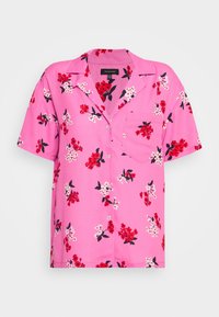 Camicetta rosa a maniche corte con motivo floreale rosso e bianco, dotata di colletto e una tasca sul petto. Realizzata in tessuto leggero.