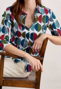 Button-up shirt featuring a white background with colorful, textured circles in red, green, blue, and teal. Short sleeves, collar visible.