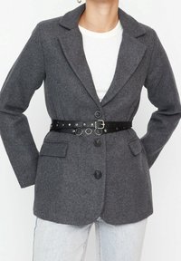 Grijze wollen blazer met gesneden revers en voorkraagzakken, vastgemaakt met een zwarte leren riem met metalen accenten en een gestructureerde pasvorm.