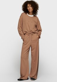 Ensemble de survêtement marron comprenant un sweat-shirt ample avec l'inscription "10 DAY" et un pantalon à jambes larges avec des bandes latérales. Tissu doux, design décontracté.