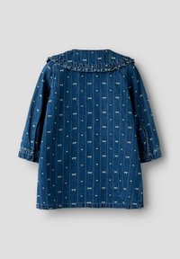 Prenda de mezclilla con un cuello volante, mangas largas y un patrón de pequeños lazos blancos sobre un fondo azul oscuro.