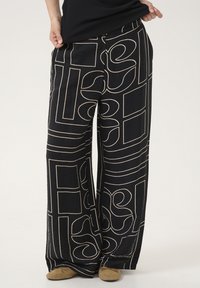Black wide-leg pants featuring cream geometric and abstract patterns with a textured fabric. Flared design extends to the ankles.