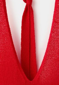 Tissu tricoté rouge à col en V profond avec une fine bretelle tricotée nouée dans le dos, texturé et légèrement transparent.