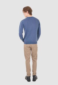 Maglione blu a coste con scollatura rotonda, abbinato a pantaloni chinos marrone chiaro e scarpe nere, mostrato da dietro su uno sfondo neutro.