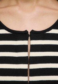 Top a righe bianche e nere in maglia con chiusure ad uncino, parzialmente allacciato, che mostra la pelle nuda all'area del collo.