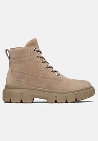 Bottine beige en daim à lacets avec semelle épaisse en caoutchouc et logo en relief sur le côté, vue de la face extérieure sur fond blanc.