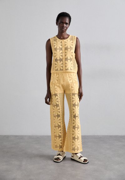 Ensemble en tricot jaune composé d'un haut sans manches avec des motifs floraux et d'un pantalon évasé, tous deux dotés d'une texture en maille ouverte.