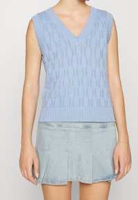 Ljust blå utan ärmar stickad väst med V-ringning, med ett strukturerat diamantsmönster och ribbad nederkant. Matchas med en denimkjol.