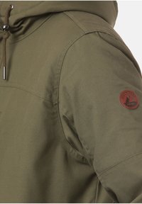 Manga de chaqueta con capucha en color verde oliva, con un parche circular de cuero marrón que presenta un diseño de montaña y el texto "LAKEVILLE MNTN".