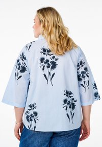 Blusa a fantasia floreale con fiori navy su uno sfondo a strisce azzurro chiaro. Presenta maniche larghe e morbide e un taglio rilassato.