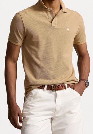 Beige polo-shirt met een gestructureerde stof, een knoopsluiting met twee knopen en een klein geborduurd logo. Draag het met witte broek en een gevlochten bruine riem.