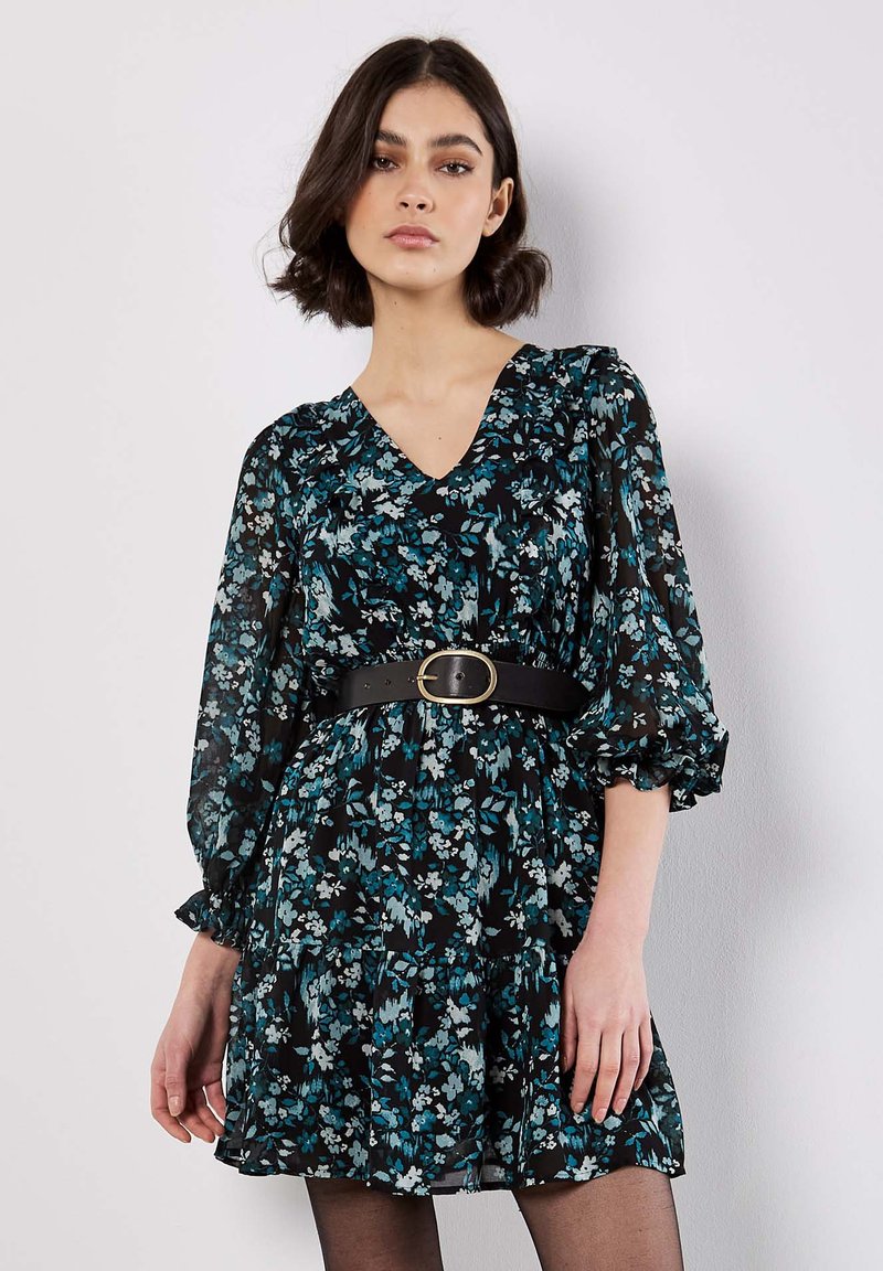 Robe noire à fleurs avec des motifs teal et blancs, décolleté en V, manches bouffantes et une ceinture noire. Le tissu est léger et texturé.