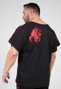 Zwarte T-shirt met korte mouwen van een gestructureerde stof, een groot rood grafisch ontwerp op de rug en rode accenten langs de schoudernaden.