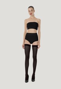 Haut bandeau noir et culotte taille haute associés à des bas noirs résille transparents montants jusqu'aux cuisses avec des bandes foncées, complétés par des talons hauts noirs.