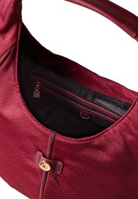 Tote in tiefrotem Farbton mit strukturiertem Äußeren, einem einzigen Griff, einem Reißverschluss-Innentäschchen und einem Metallschließe-Detail.