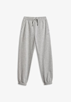 Enfant debout portant un sweat à capuche gris zippé, un pantalon de jogging assorti, un t-shirt bleu et des baskets noires et blanches sur un fond uni.