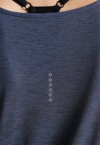 Námořnická modrá blůza s hladkým, texturovaným materiálem, která má pět malých, kulatých knoflíkových detailů uspořádaných vertikálně uprostřed.