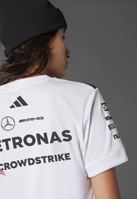 Camiseta deportiva blanca con acentos negros, que presenta logos de patrocinadores como Petronas y Crowdstrike. Fabricada con un tejido suave y transpirable.