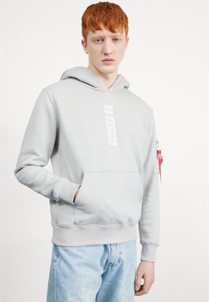 Grå bomulds-hoodie med en frontlomme, et stort logo på brystet og en sidelomme med lynlås, der har et rødt mærke. Blød tekstur og afslappet design.