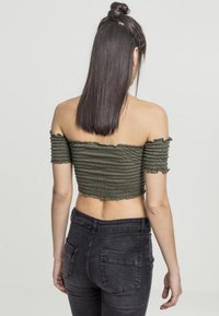 Olivenfarget, off-shoulder cropped topp med ribbestruktur og korte pufferm, brukt sammen med høytlivde svarte jeans.