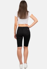 Bermudas en denim noir avec une coupe près du corps, taille mi-haute et ourlets retournés, associées à un crop top blanc et des baskets blanches.