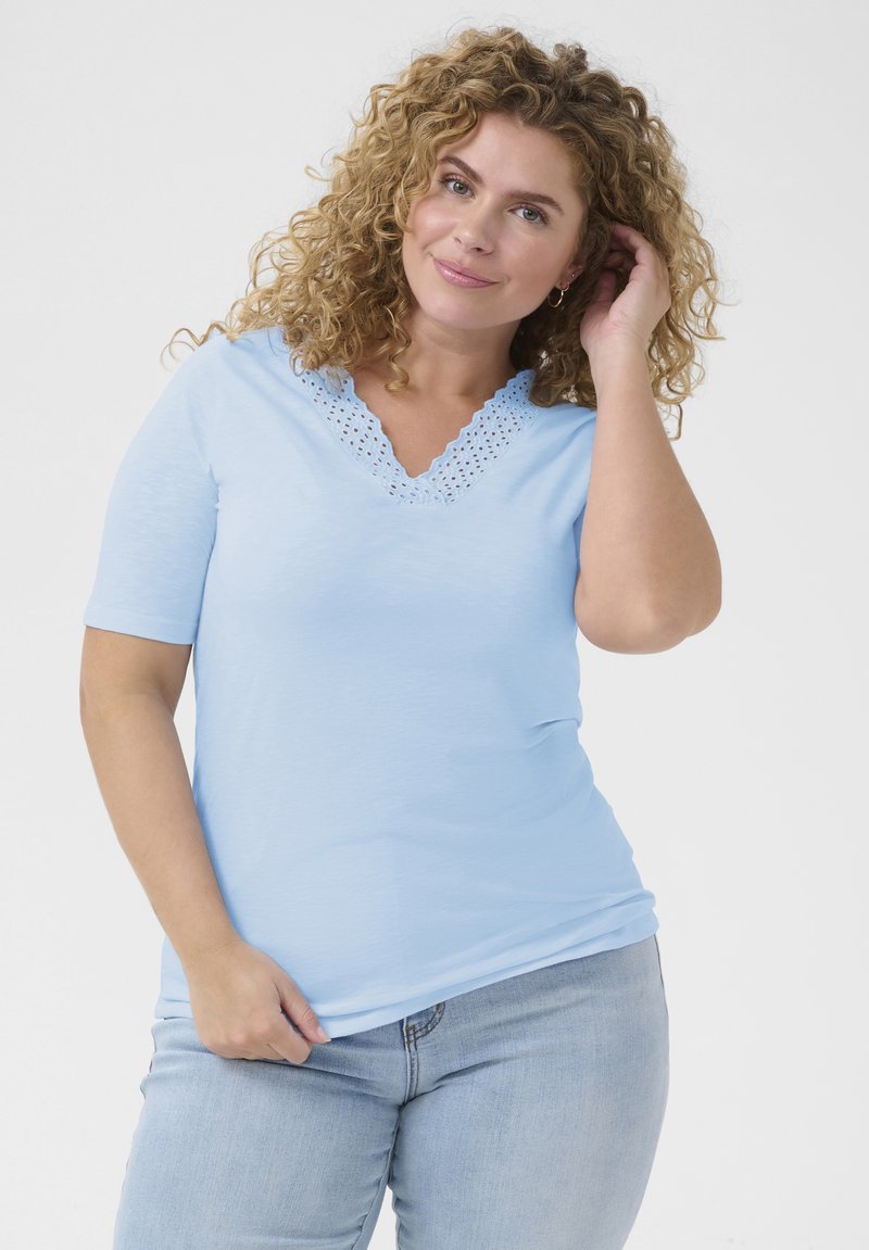 Top azul claro de manga corta con escote en V y detalles de encaje recortados. Tela suave, corte holgado, combinado con jeans de mezclilla claros.