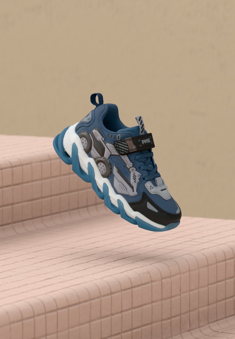 Blue and gray sneaker featuring a textured upper, black accents, chunky white midsole, and a strap with logo, suspended above a pink tiled surface.