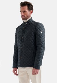 Gequilted marineblauwe jas metstaande kraag, drukknoopsluiting en zijzakken. Kenmerkt zich door een gestructureerd, gewatteerd ontwerp en een subtiele metalen logo-accent.