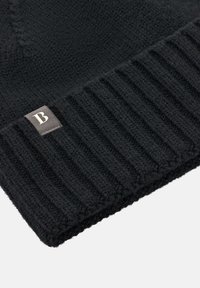 Čierna pletená čiapka s ryhovaným vzorom. Obsahuje malú obdĺžnikovú nášivku s bledoprsitým písmenom "B". Mäkka textúra.