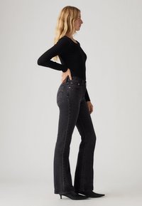 Jean flare noir à taille haute, avec une légère texture et des coutures classiques. Associé à un haut noir ajusté à manches longues.