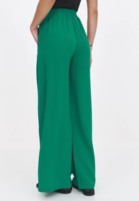 Zielone spodnie o szerokich nogawkach z teksturowanej tkaniny i elastycznym paskiem w talii. Charakteryzują się luźnym krojem, bocznymi szwami i lekko rozszerzanym dołem.